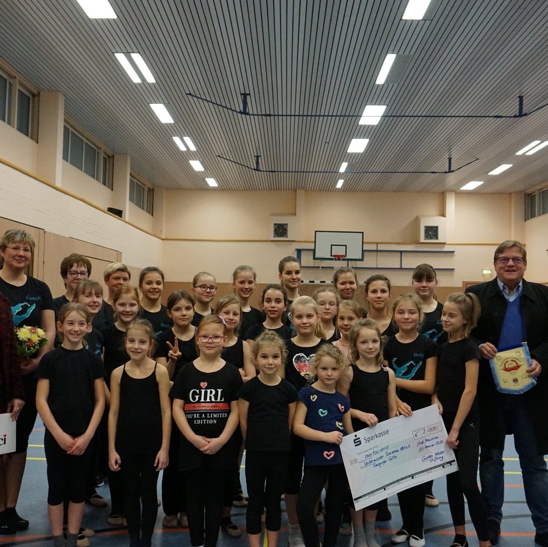 Eine Gruppe Kinder steht in Sportkleidung in einer Turnhalle, sie erhalten gerade einen Spende