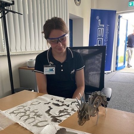 Eine weibliche Person sitzt vor einem Dinosaurier Skelett aus Metall