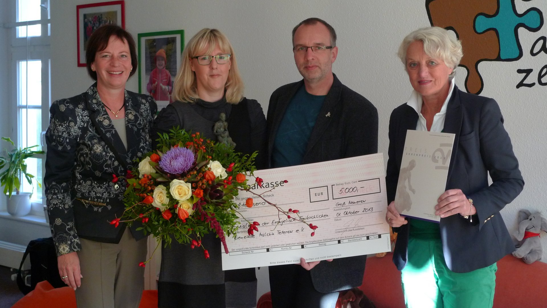 Vier Personen, drei Frauen ein Mann, halten einen Check in die Kamera