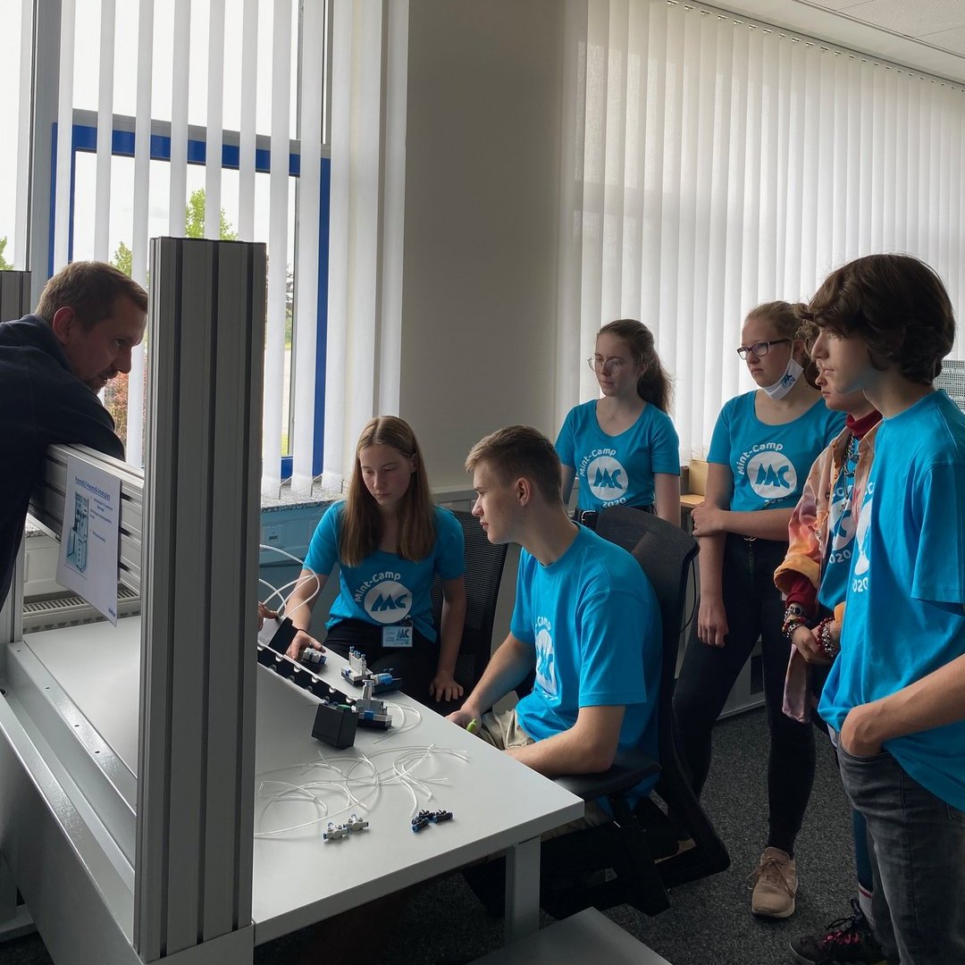 Jugendlich stehen um einen Tisch während ein Mann etwas an einer Technischen Anlage erklärt